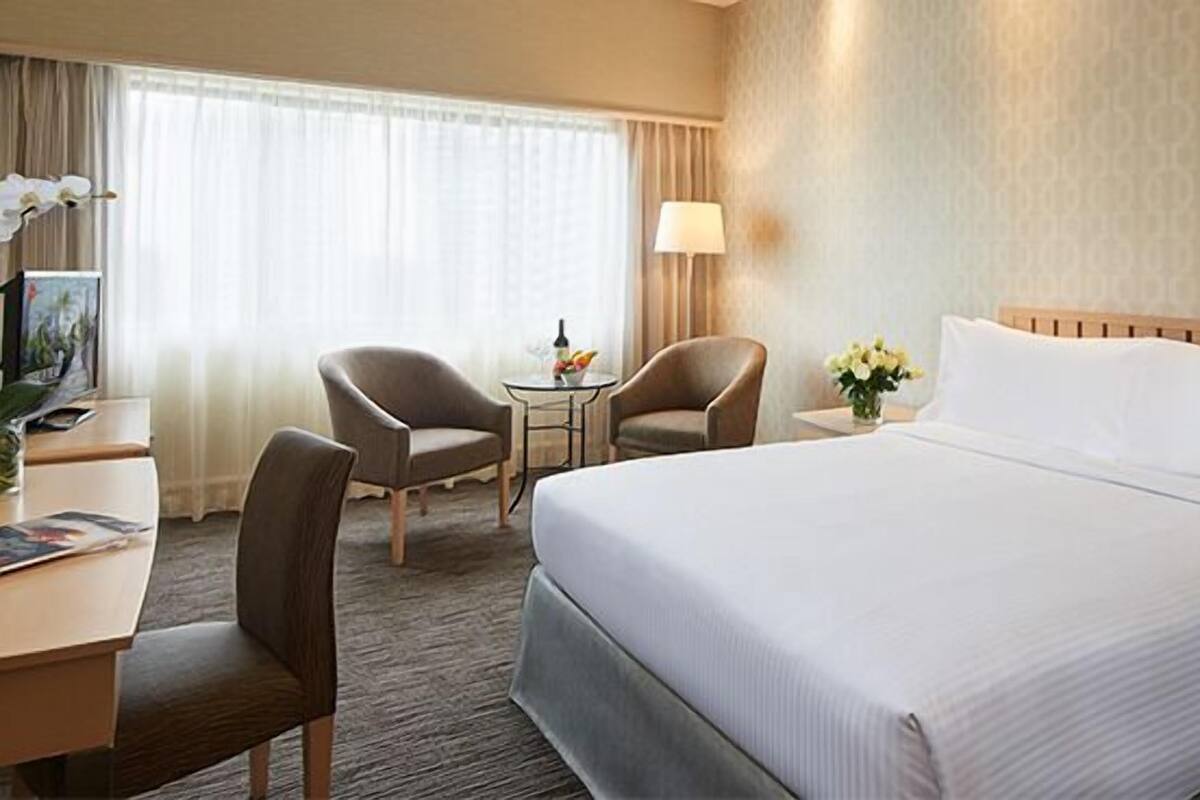 A hotel room with a large bed, two armchairs, a small table with a lamp, and a TV.
