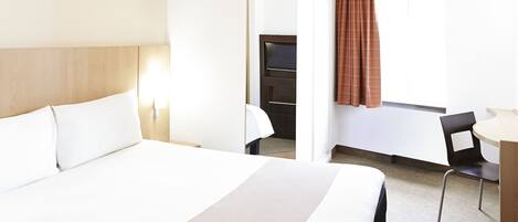 A hotel room with a large bed, a desk, and a chair.