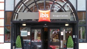 The exterior of the ibis Birmingham City Centre hotel with a prominent red and white sign, large windows, and two symmetrical potted plants at the entrance. - Ibis Birmingham New Street Station Hotel (Birmingham)