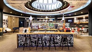 A modern bar area with a circular ceiling design, a bar counter, stools, and a pizza menu. - Ibis Birmingham New Street Station Hotel (Birmingham)