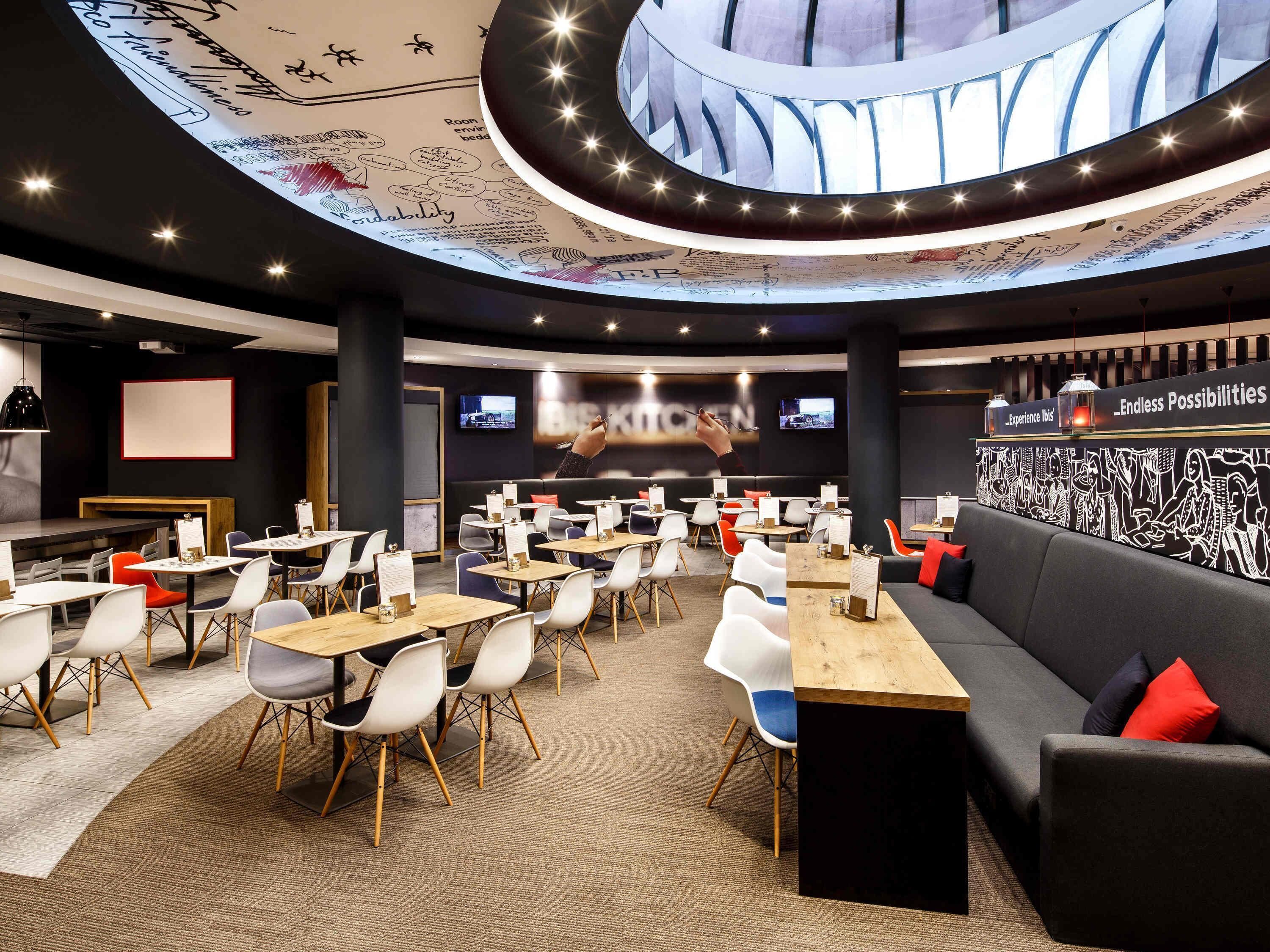 Een moderne eetruimte met ronde tafels en stoelen, een bar en een groot scherm waarop een presentatie wordt getoond.