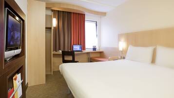 A hotel room with a large bed, a desk with a laptop, a TV, and a small seating area.