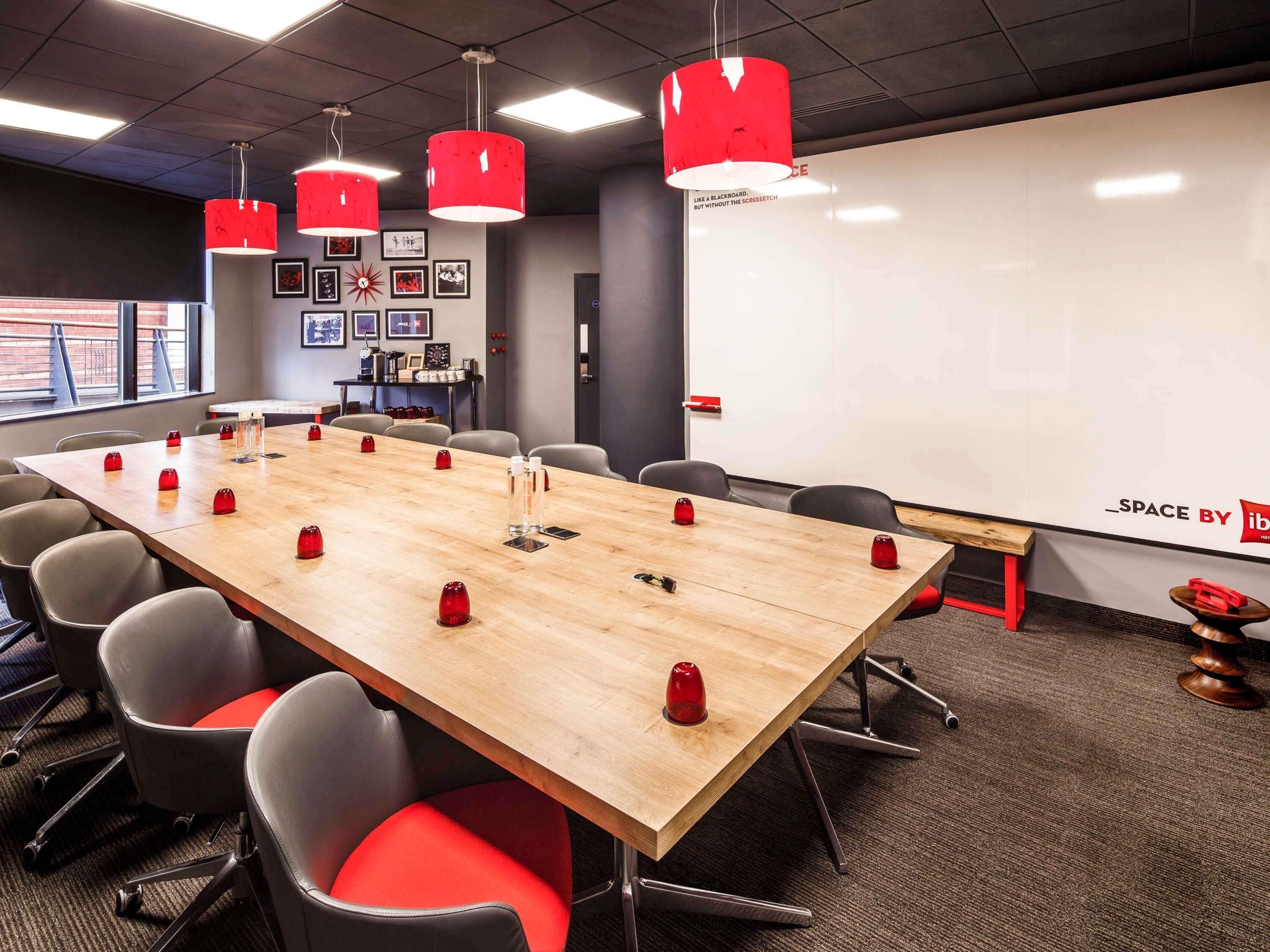 A conference room with a long wooden table, red chairs, and a whiteboard.