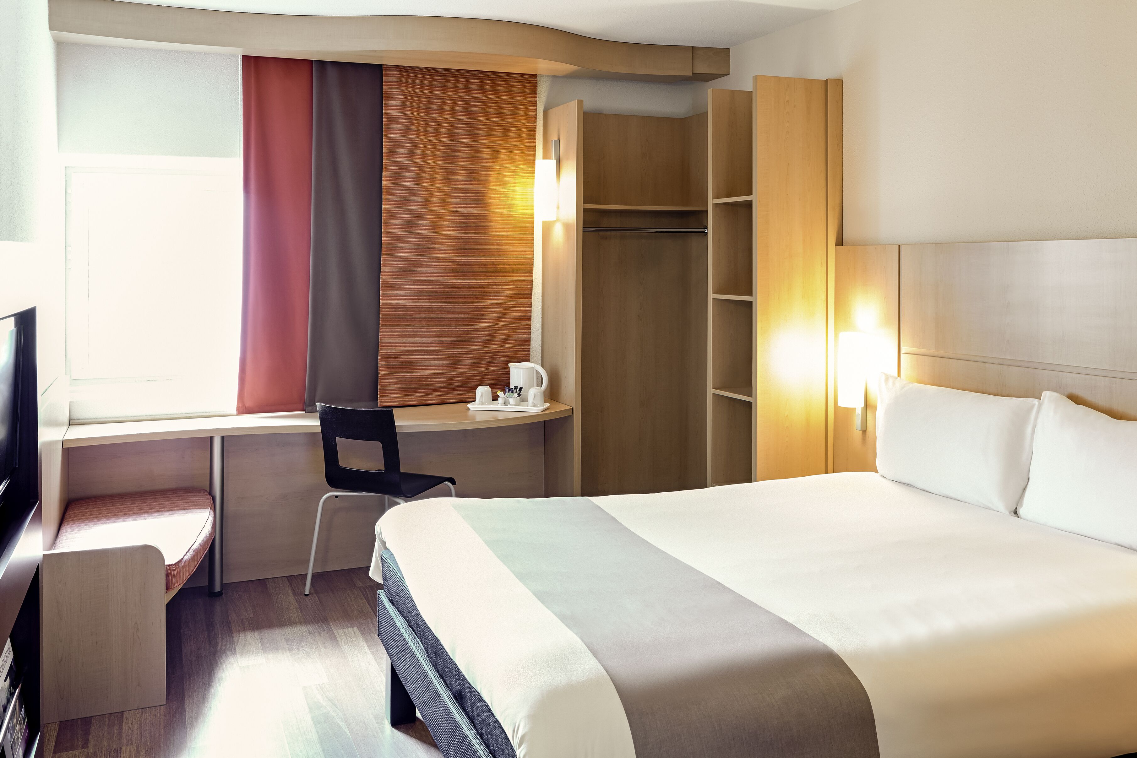 Ein Hotelzimmer mit Bett, Schreibtisch, Stuhl und Kleiderschrank.