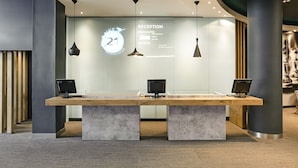 A reception desk with two monitors, a digital display with room rates, and a modern interior design. - Ibis Birmingham New Street Station Hotel (Birmingham)