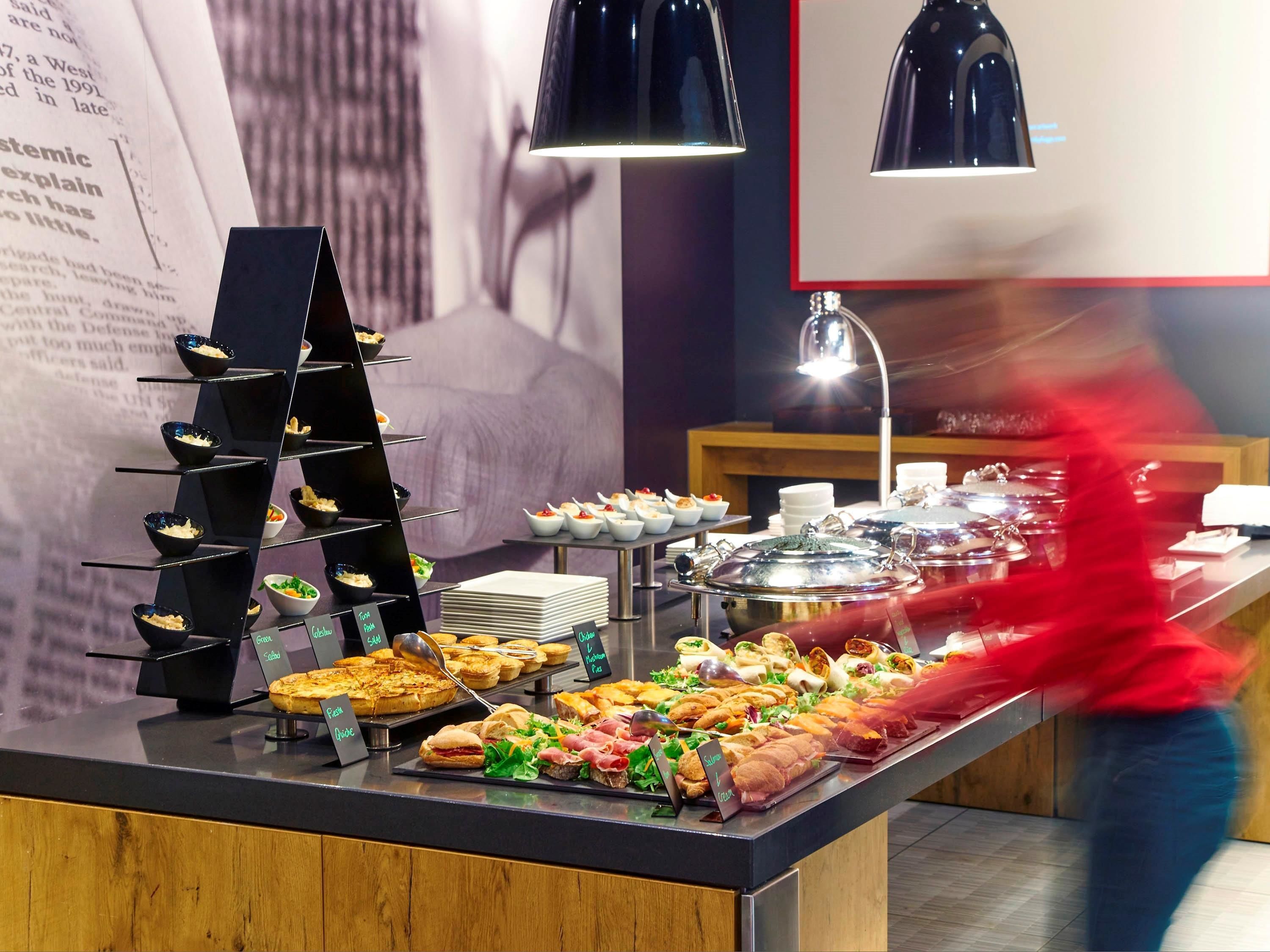 A buffet with various food items and a person in a red shirt walking by.