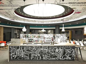 Zona de bar moderna amb un disseny de sostre circular, un taulell de bar amb un mural en blanc i negre, i diverses llums penjants.
