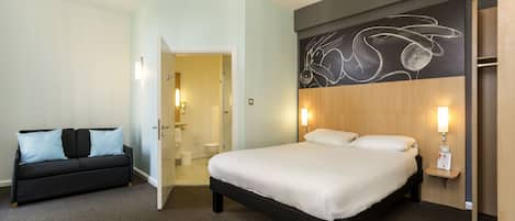 A hotel room with a bed, a sofa, a bathroom, and a wall with a chalkboard design.