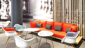 A modern lounge area with a red sofa, white and blue chairs, and a small table. - Ibis Birmingham New Street Station Hotel (Birmingham)