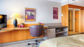 Habitación de hotel con cama, escritorio con lámpara, una silla, televisor y obras de arte en las paredes.