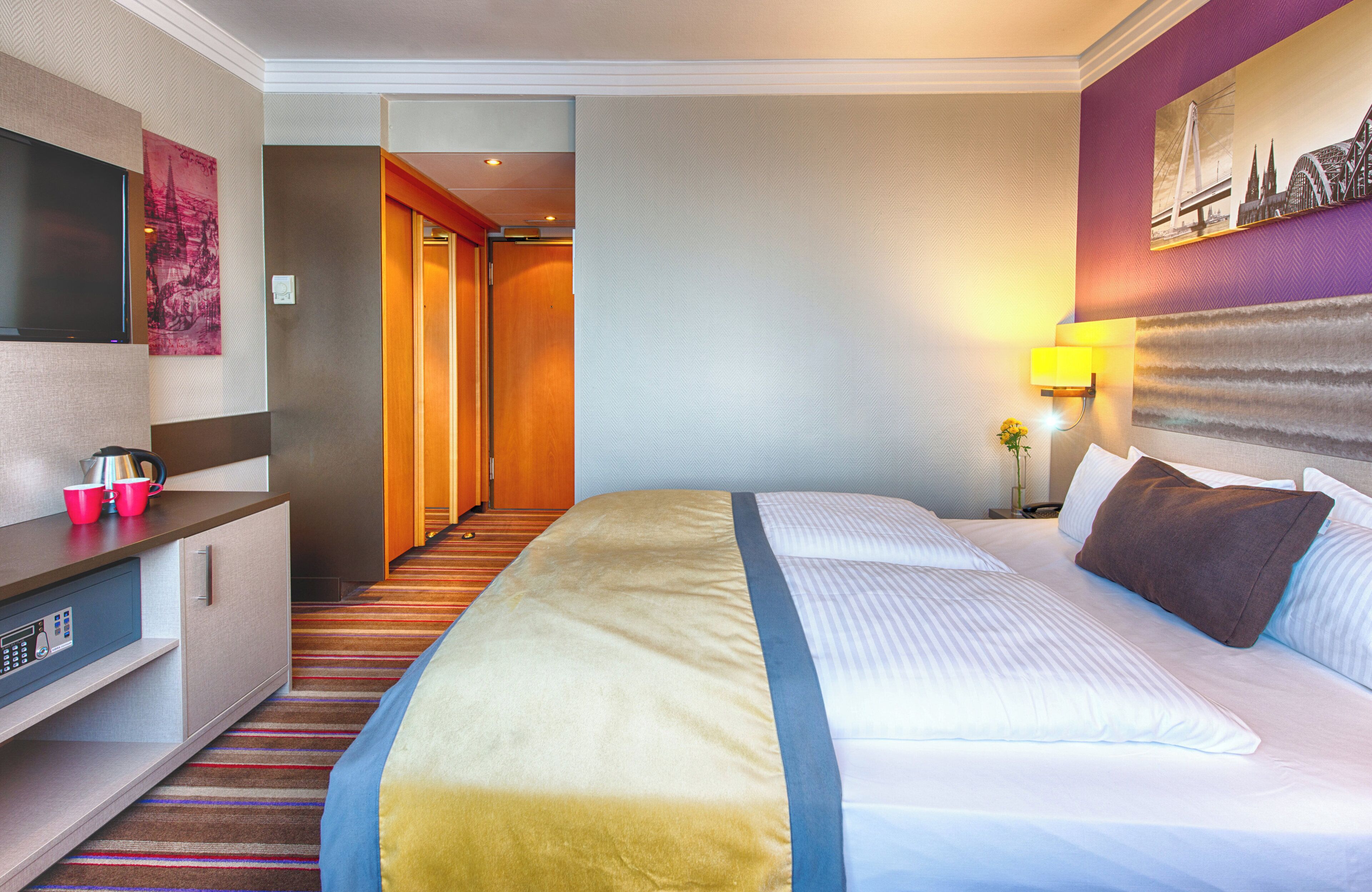 A hotel room with a large bed, a desk with a computer, a TV, and a painting on the wall.
