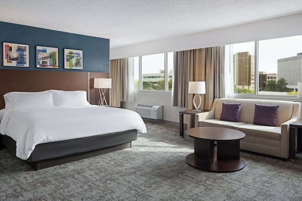 A hotel room with a large bed, a sofa, a coffee table, and a view of the city.