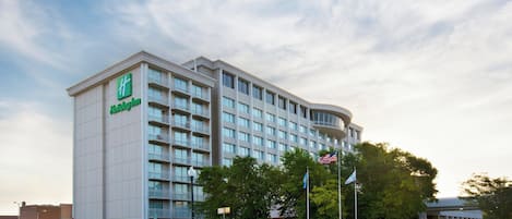 A Holiday Inn hotel with a modern design, multiple floors, and a parking lot with various vehicles.