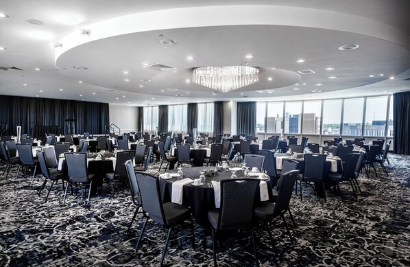 A large conference room with round tables and chairs, a chandelier, and large windows offering a city view. - Holiday Inn Sioux Falls-City Centre by IHG (Sioux Falls)