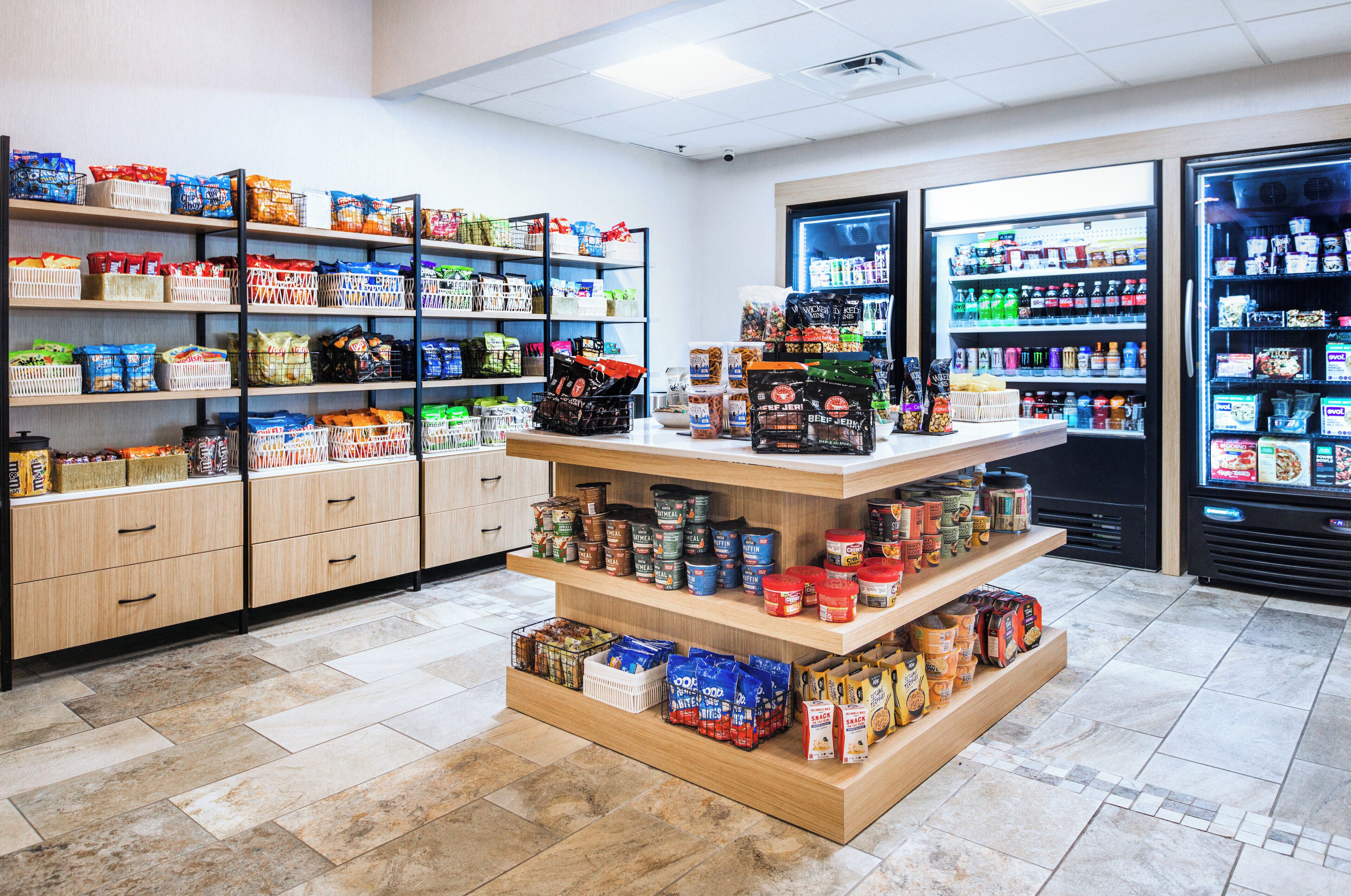 A grocery store with shelves stocked with various food items, a refrigerated section, and a display counter with packaged goods.