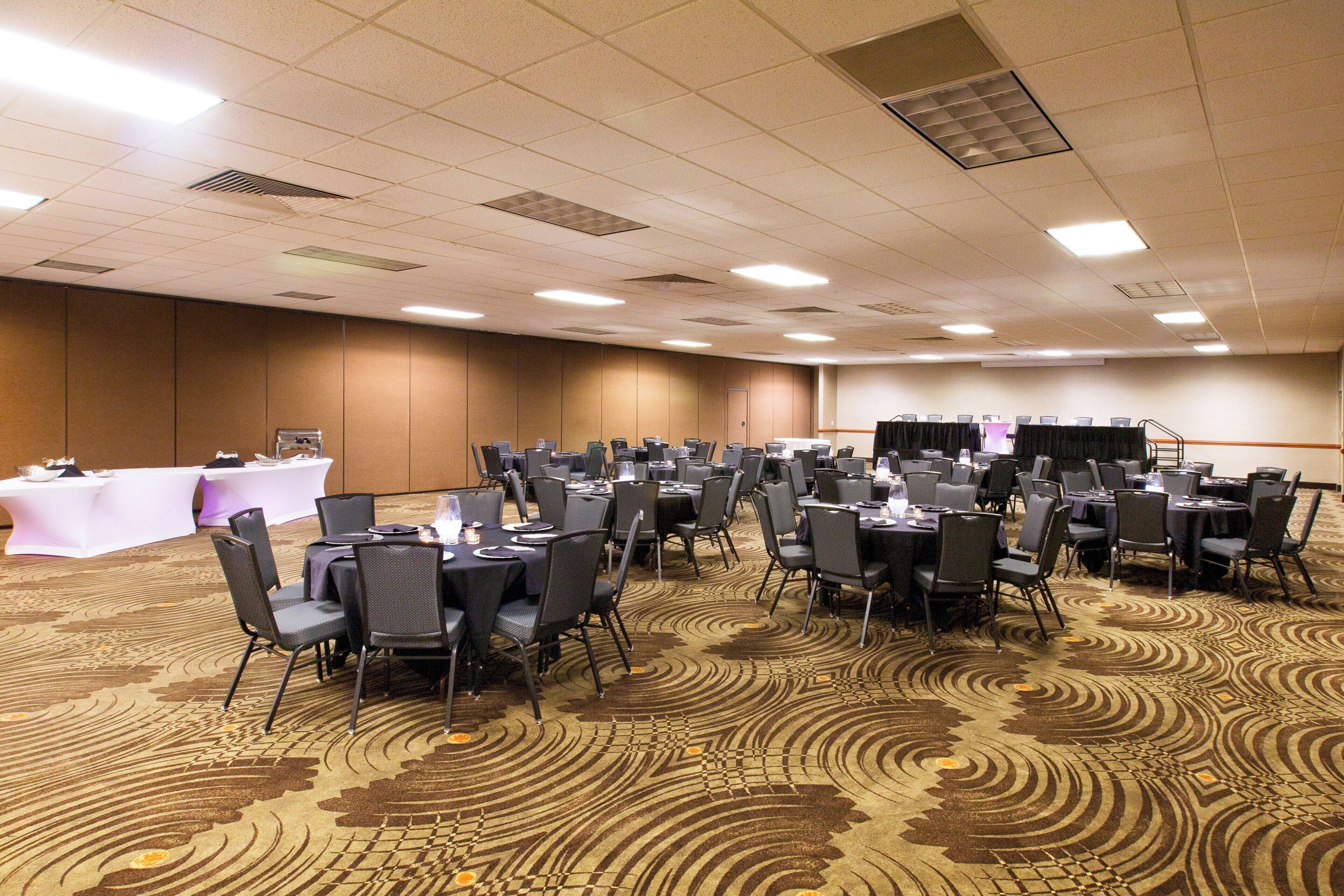A conference room with multiple tables and chairs, carpeted floor, and ceiling vents.