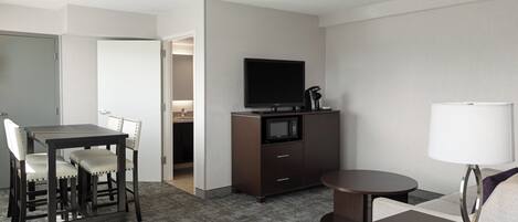Habitación de hotel con una mesa de comedor, sillas, televisor, microondas, lámpara y sofá.