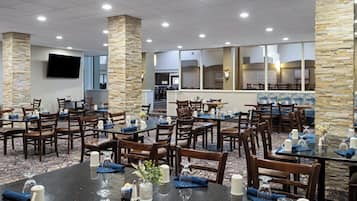 Un espace de restauration d’hôtel comprenant plusieurs tables et chaises, des piliers en pierre et un téléviseur à écran plat fixé au mur.