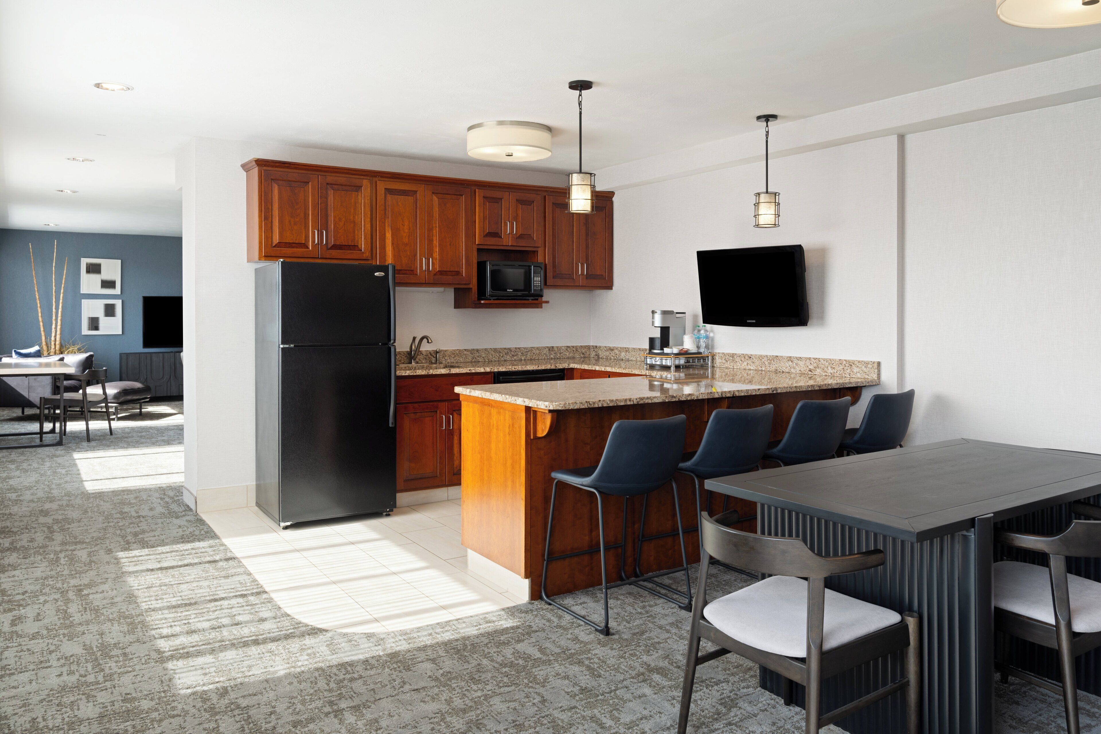 A modern kitchen with wooden cabinets, a black refrigerator, a microwave, and a built-in island with bar stools.