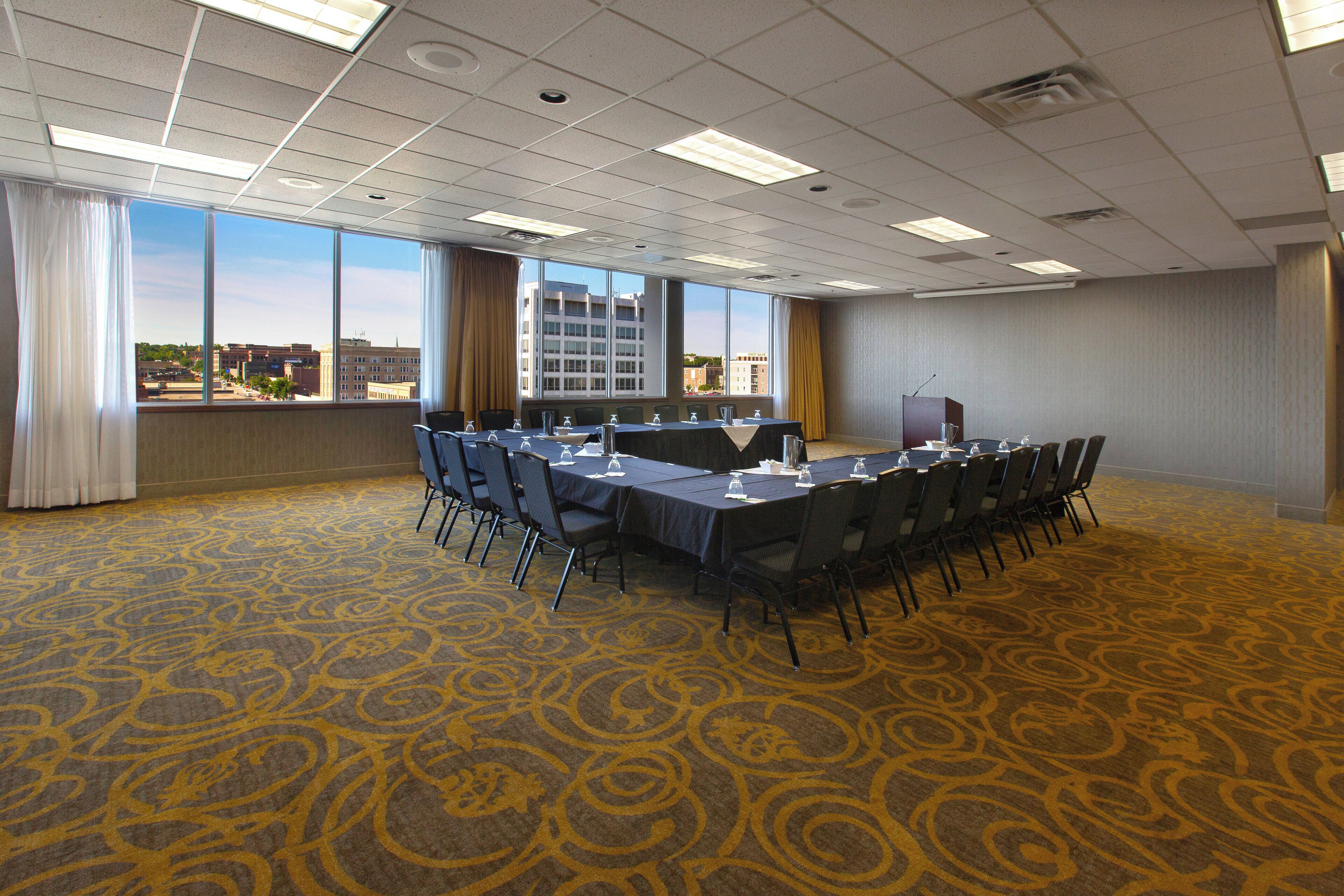 A conference room with a long table, chairs, and a view of a cityscape through large windows.
