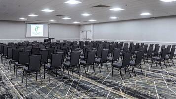 A conference room with rows of chairs, a projector screen, and a carpeted floor.