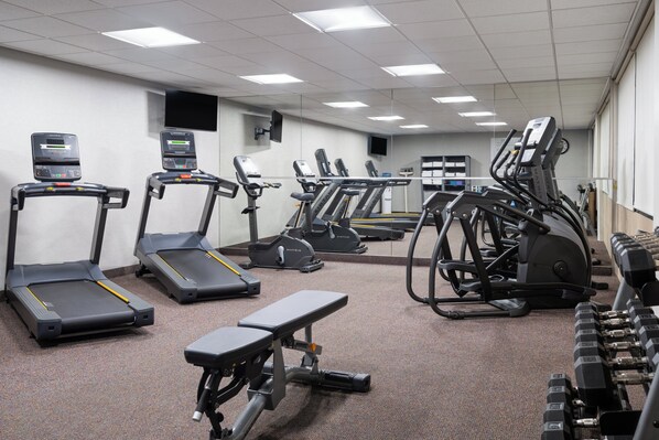 Une salle de sport équipée de tapis de course, de vélos elliptiques et d’haltères.