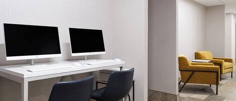Een moderne kantoorruimte met twee computerbeeldschermen op een wit bureau, twee donkere stoelen en een gele fauteuil op de achtergrond.