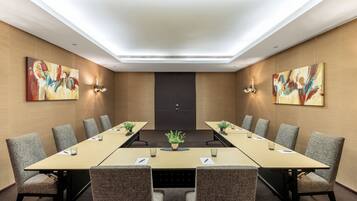 Une salle de conférence avec une longue table, des chaises et deux tableaux accrochés aux murs.