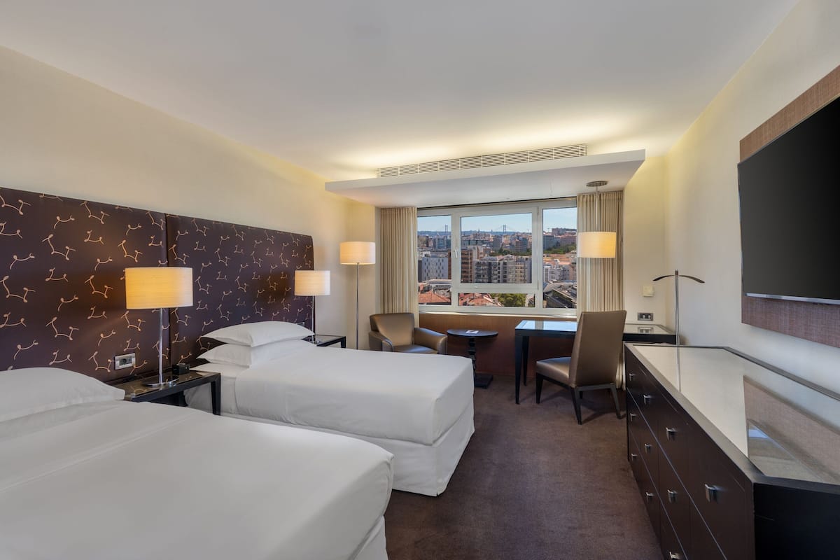 Habitación de hotel con dos camas, un escritorio, una silla, un televisor y vistas a la ciudad.