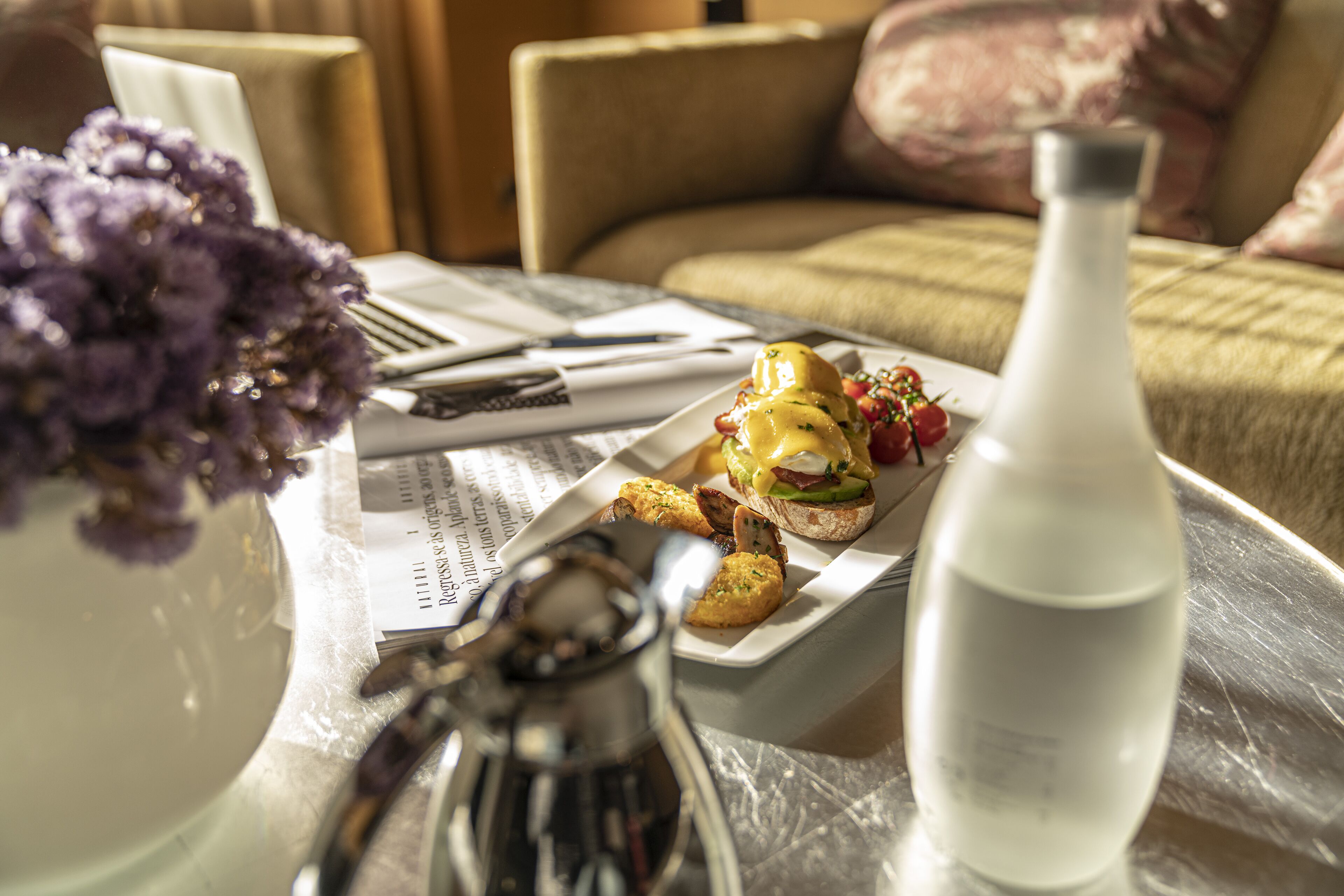 Una mesa de comedor con comida, un salero, una botella de agua y un florero.