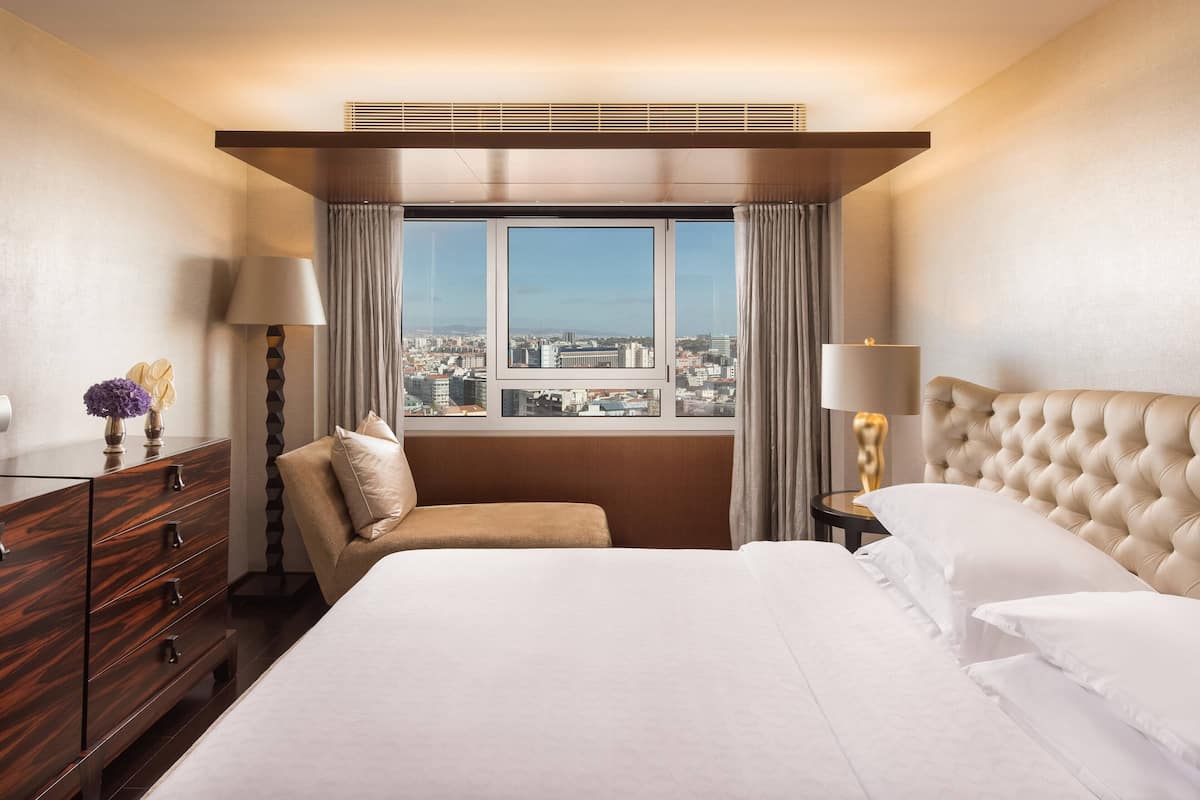 Habitación de hotel con una cama grande, una silla, un aparador y una ventana con vista a la ciudad.