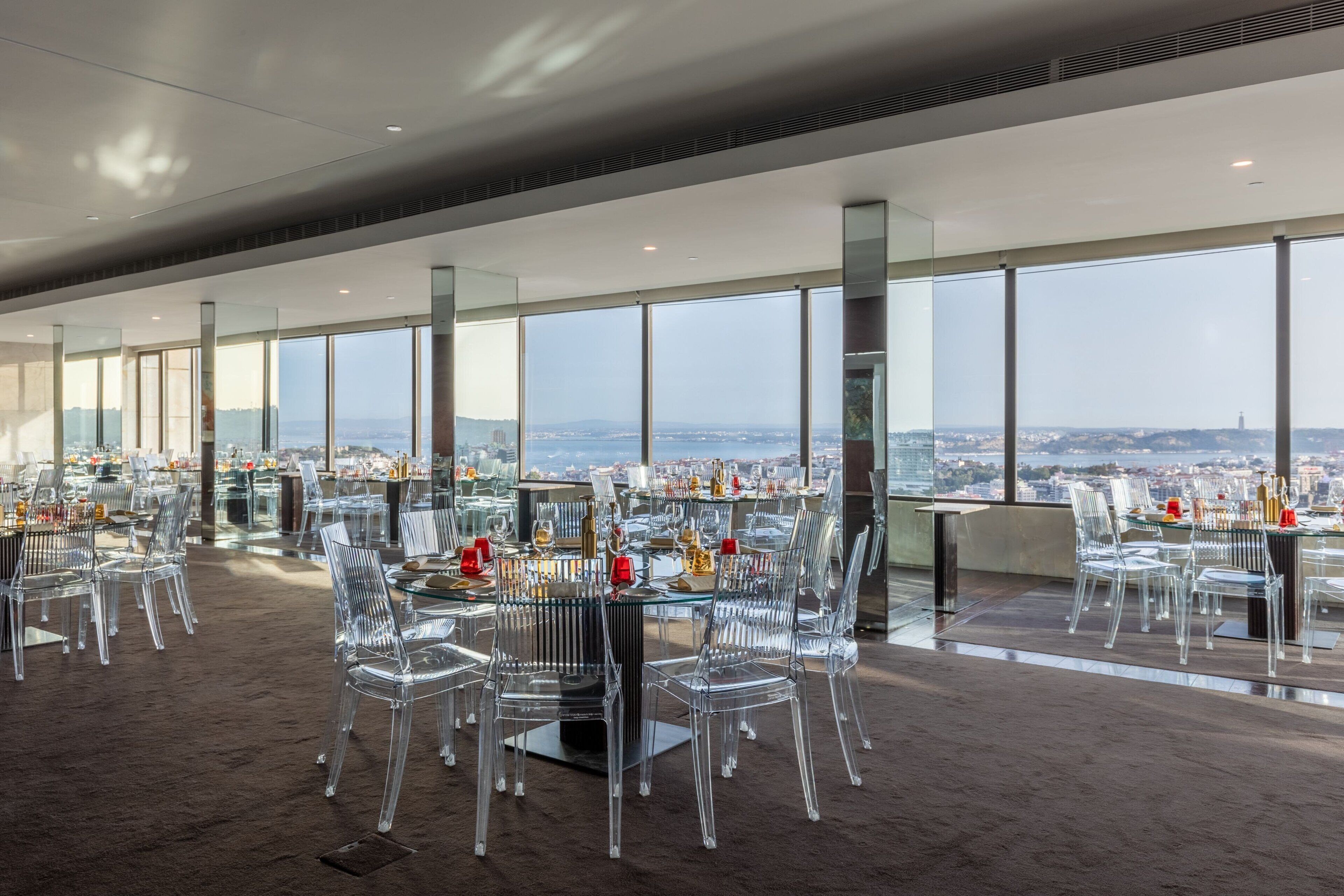 A modern dining area with clear glass chairs and tables, large windows offering a city view.