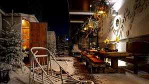 Un espacio exterior cubierto de nieve con un columpio de madera, una mesa de comedor con bancos y un árbol de Navidad.