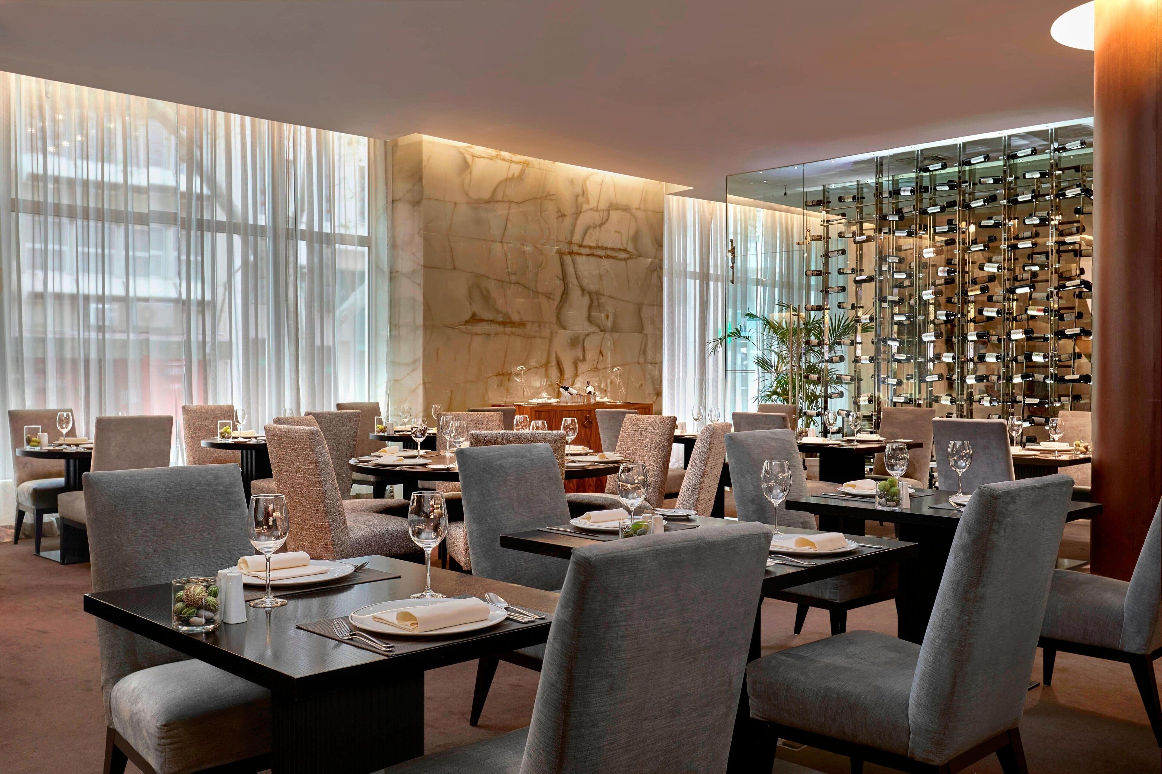Un restaurant avec des tables dressées, un mur en marbre et un présentoir à vin.