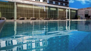 Una piscina con sillones de descanso y un edificio con grandes ventanales al fondo.