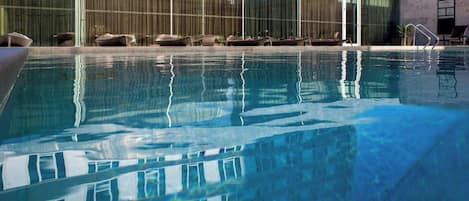 A swimming pool with lounge chairs and a building with large windows in the background.