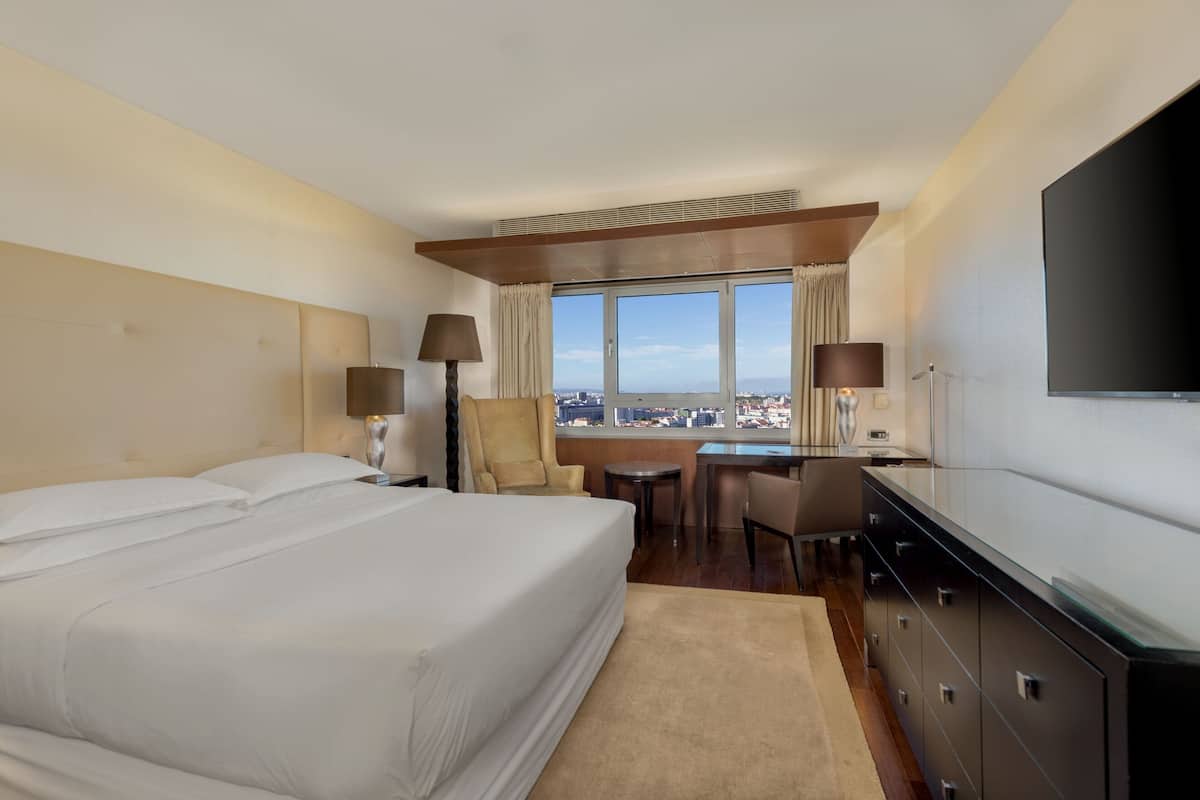 Habitación de hotel con una cama grande, un escritorio, dos sillas, un televisor y vistas a la ciudad.