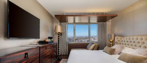Una habitación de hotel moderna con una cama grande, un televisor de pantalla plana, un aparador de madera y vistas a la ciudad a través de la ventana.