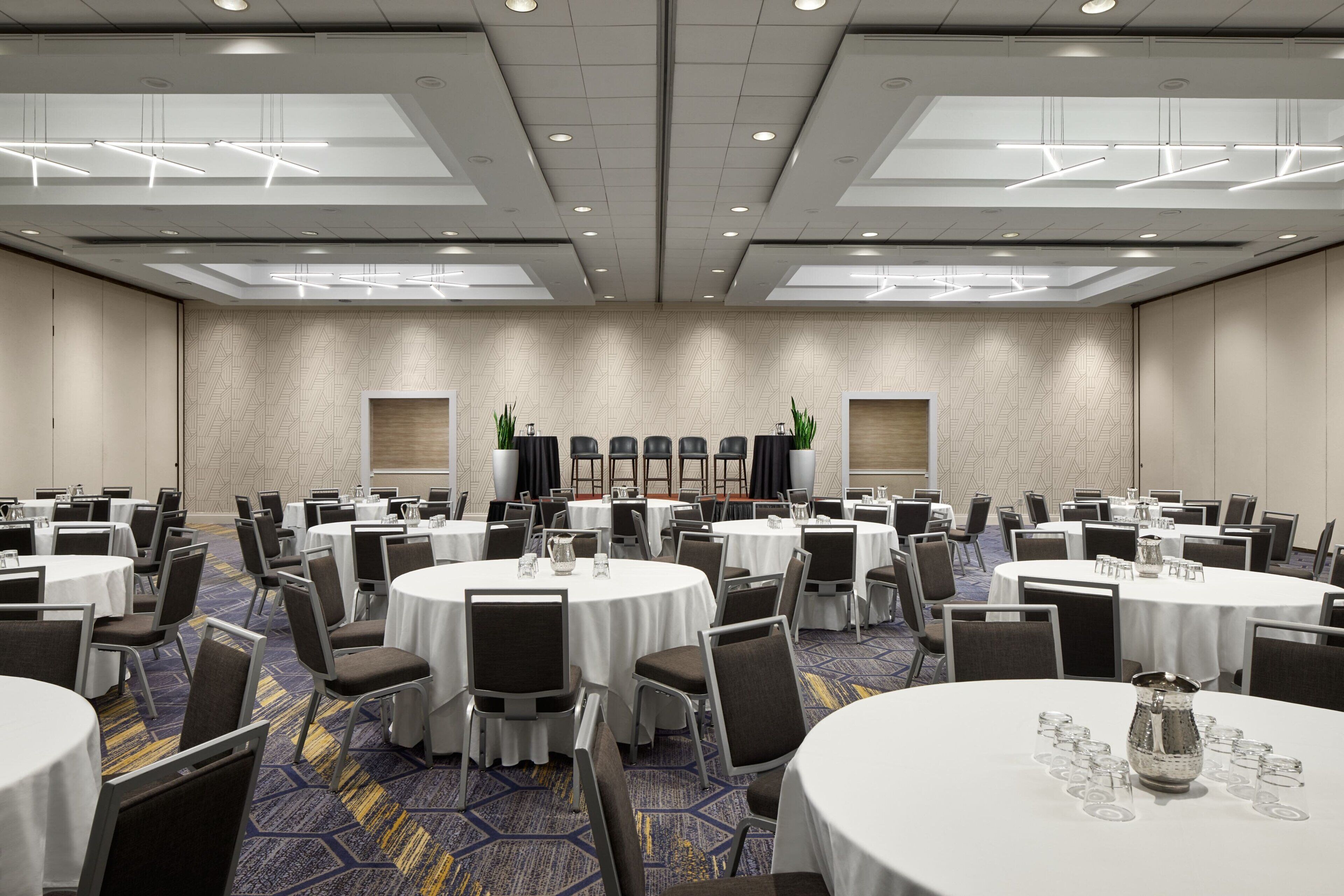 Un salón de conferencias con mesas redondas, sillas y una alfombra estampada.