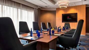 A conference room with a long table, black chairs, blue water bottles, and a TV screen displaying the Marriott logo.