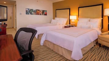 A hotel room with two beds, a desk, and a chair. There are two bedside tables with lamps.