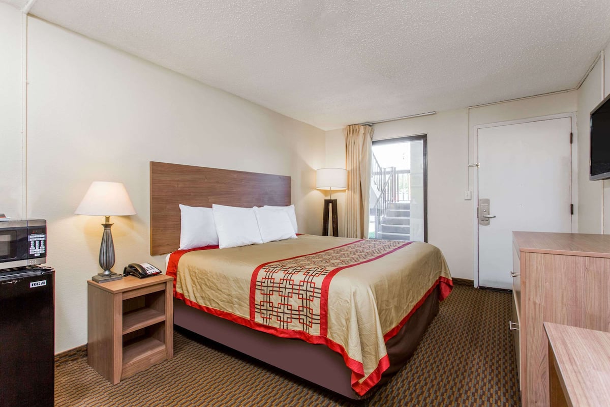 A hotel room with a bed, bedside lamps, a TV, a desk, and a microwave.
