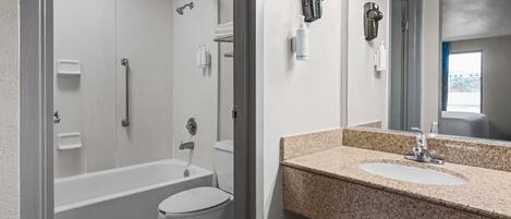 A bathroom with a bathtub, toilet, and a sink with a granite countertop.