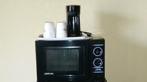 Un refrigerador negro con un microondas encima, un cable de alimentación conectado y un piso con diseño de ladrillos.