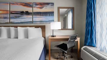 Una habitación de hotel con cama, escritorio, silla y un ventanal con cortinas.