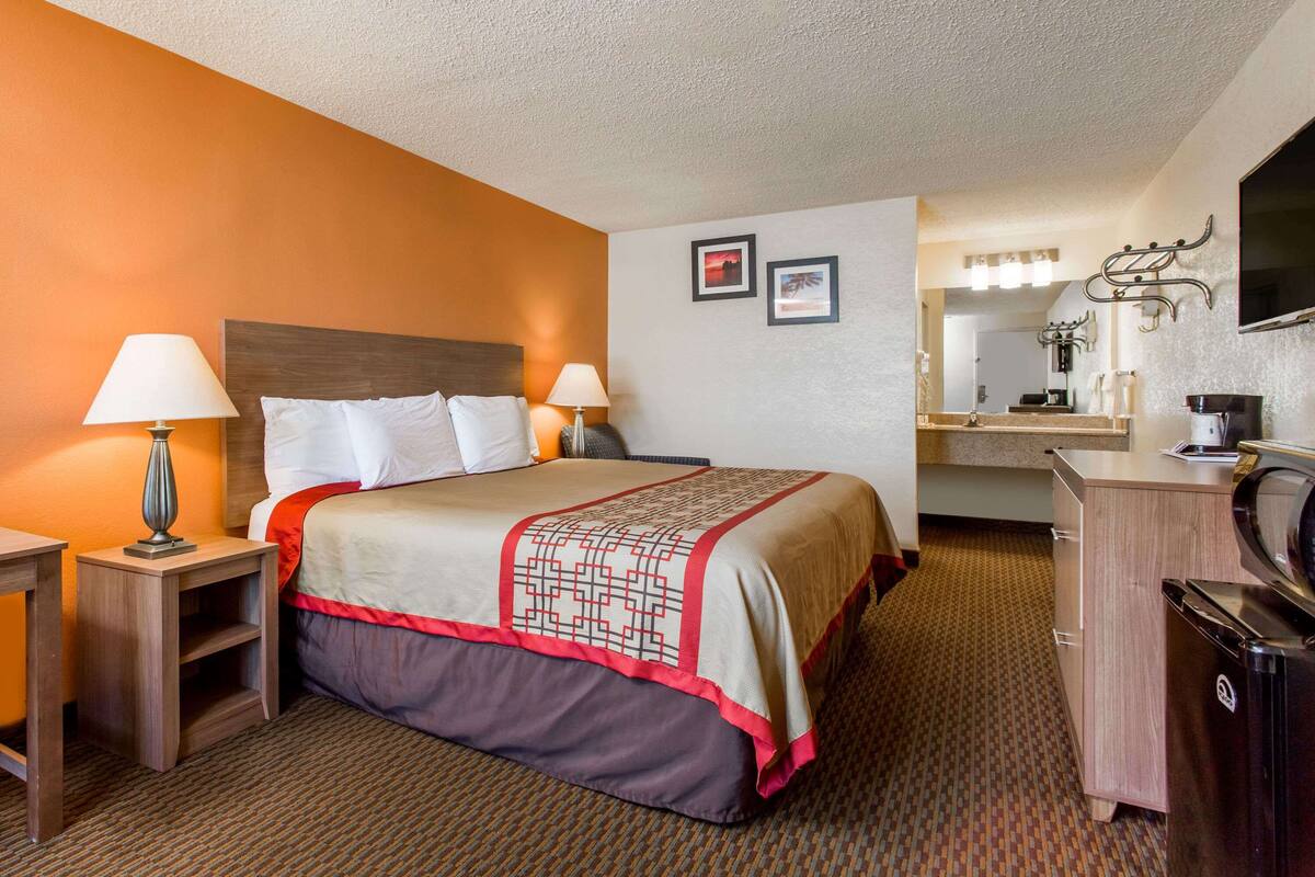 A hotel room with a bed, bedside tables, a desk, a mirror, and a television.
