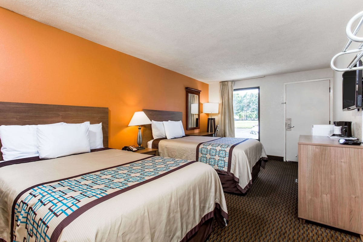 A hotel room with two beds, a desk, a mirror, and a window.