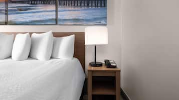 Hotelkamer met een bed, kussens, een nachtkastje met een lamp en telefoon, en een schilderij van een pier en de oceaan.