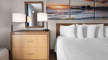A hotel room with a bed, a wooden dresser with drawers, a large mirror, and a wall-mounted lamp.