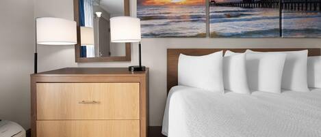 Habitación de hotel con cama, cómoda de madera con cajones, un espejo grande y una lámpara fijada a la pared.